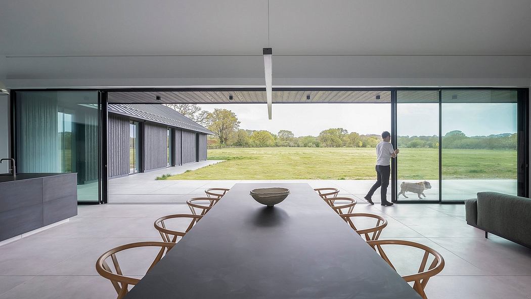 Minimalist modern interior with expansive glass walls overlooking a grassy field.