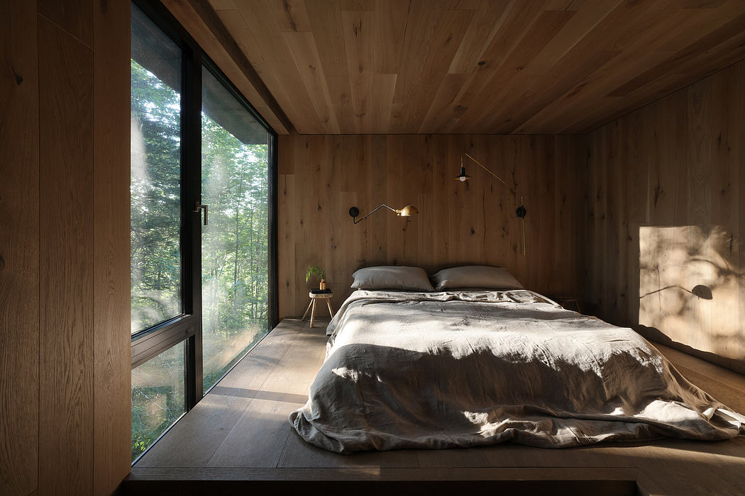 Cozy wood-paneled bedroom with large wall-to-wall window overlooking lush greenery.