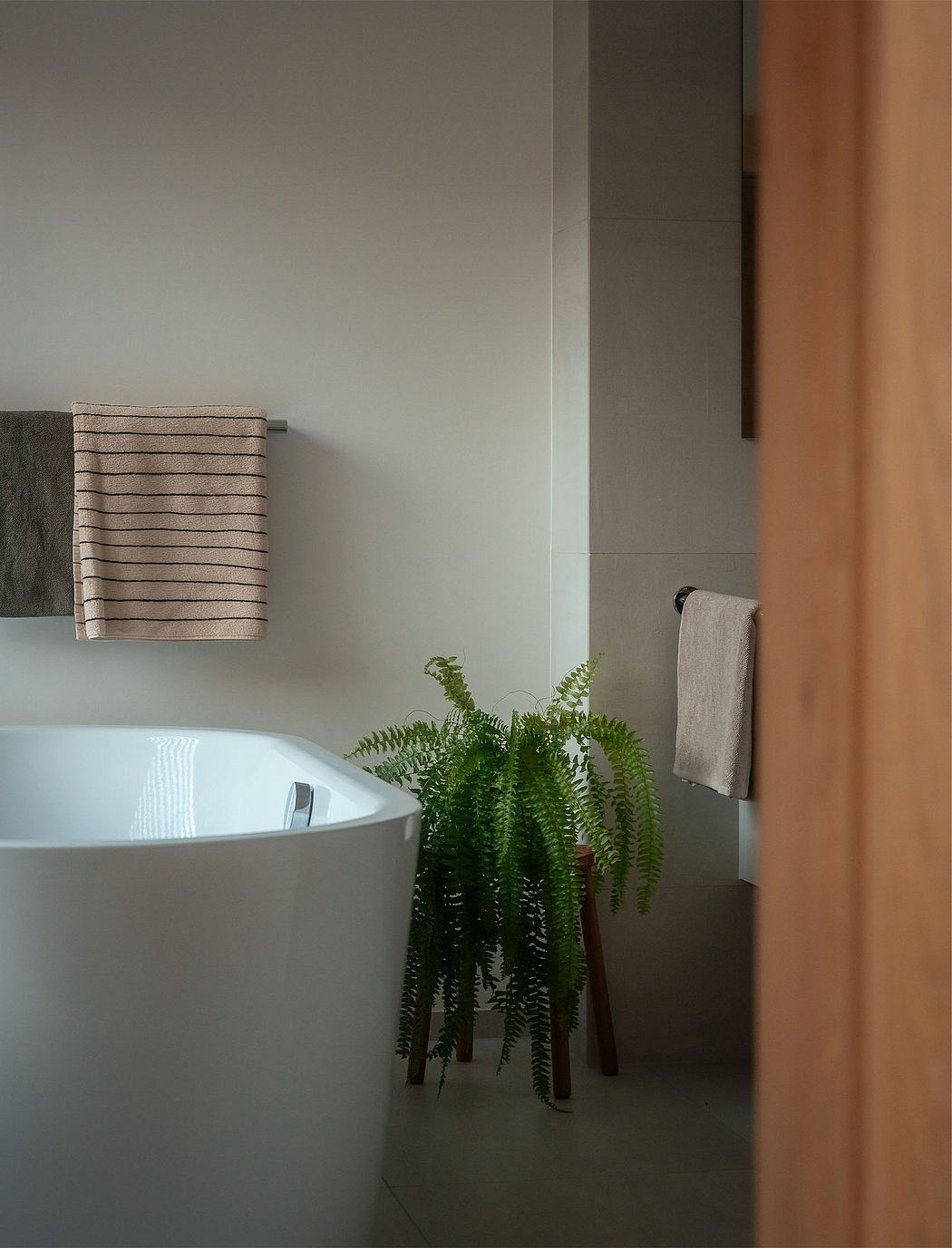 A minimalist bathroom with a freestanding tub, towels, and potted ferns creating a serene, natural atmosphere.