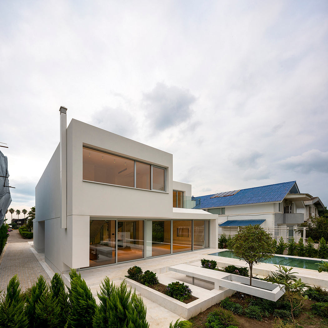 Modern, minimalist home with expansive glass walls, blue steel roof, and well-landscaped exterior.