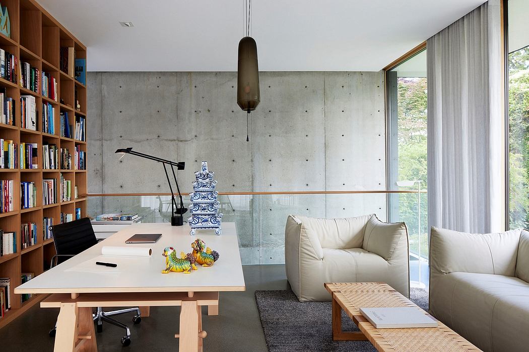 A modern home office with concrete walls, wooden shelves, and a glass wall overlooking nature.