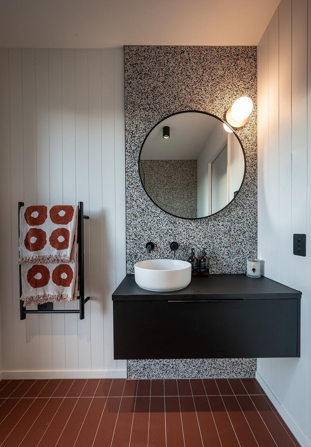 A modern bathroom with a textured granite wall, round mirror, and black vanity.
