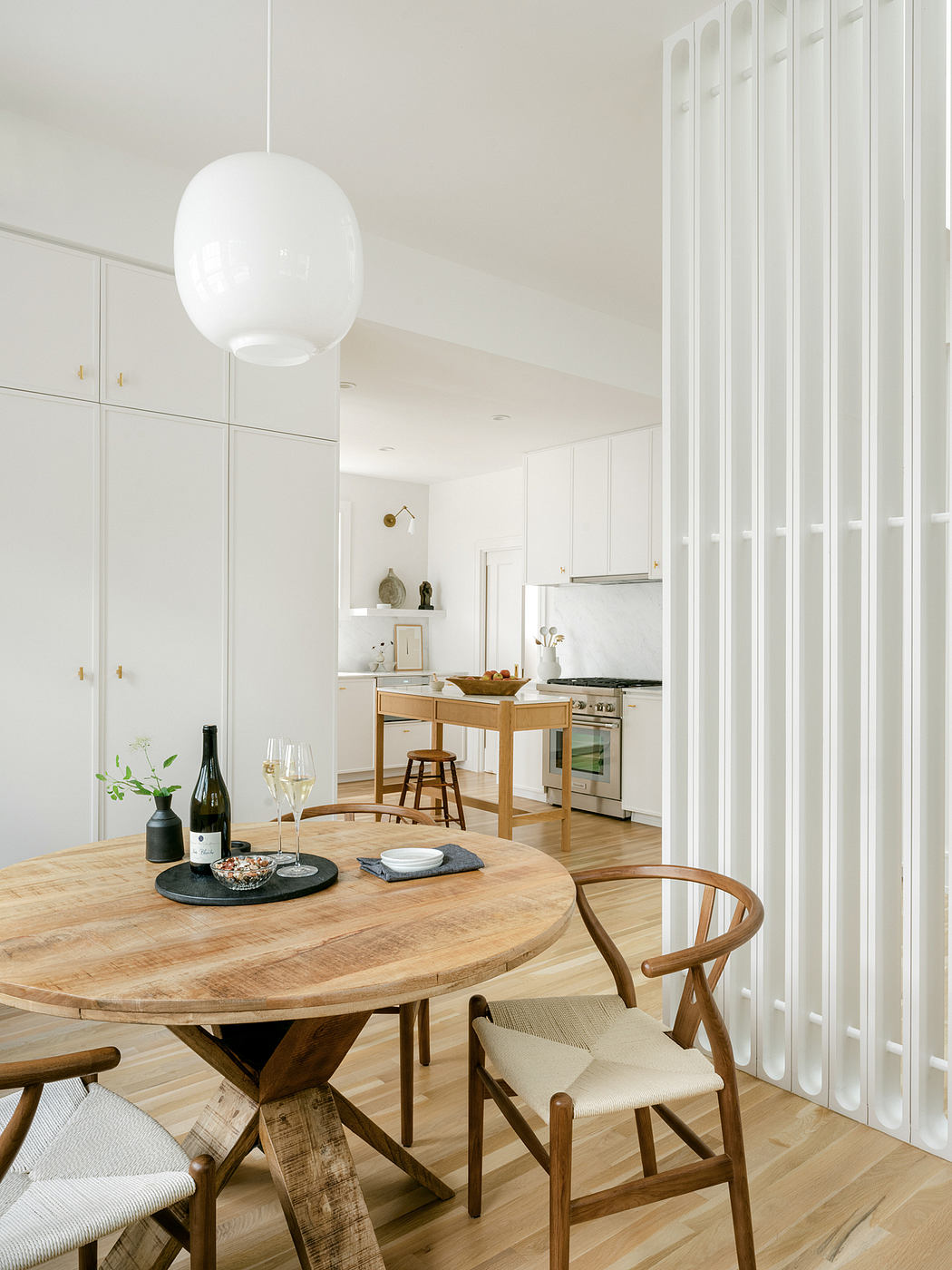 A modern kitchen and dining space with a large round wooden table and white cabinetry.