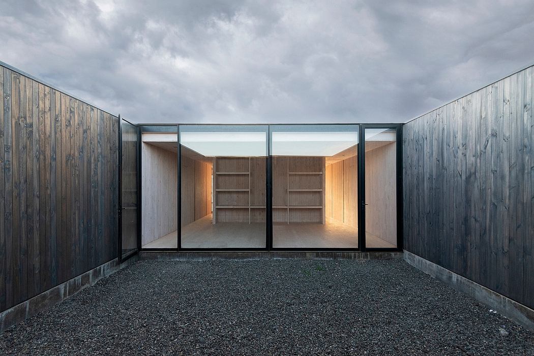 A minimalist, open-plan structure with wooden walls, glass panels, and built-in shelves.