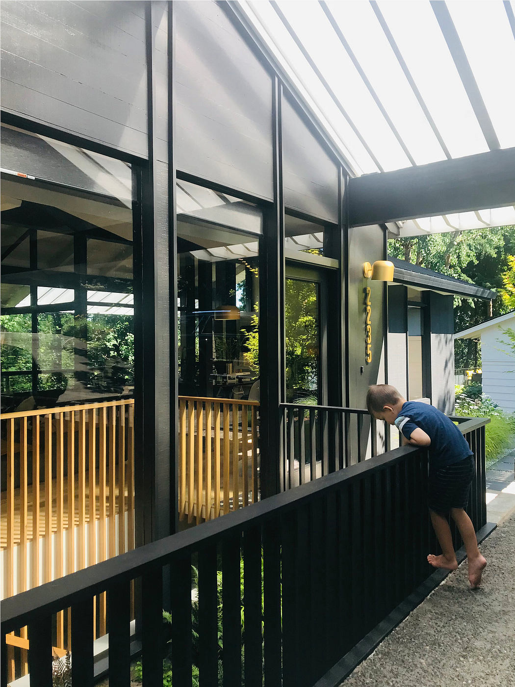Contemporary architecture with glass walls, wooden railings, and an outdoor deck overlooking lush greenery.