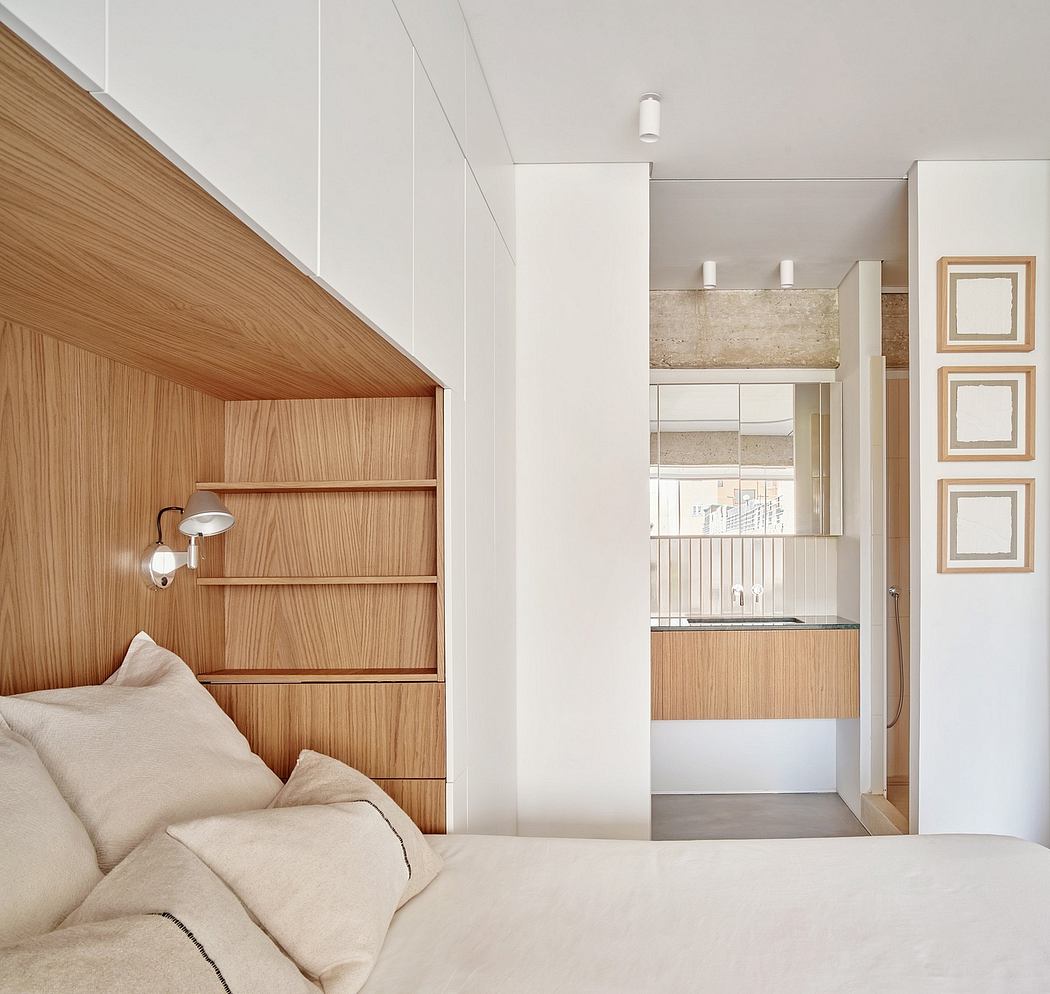 Minimalist bedroom with wooden built-in shelving, neutral palette, and glimpse of kitchen.