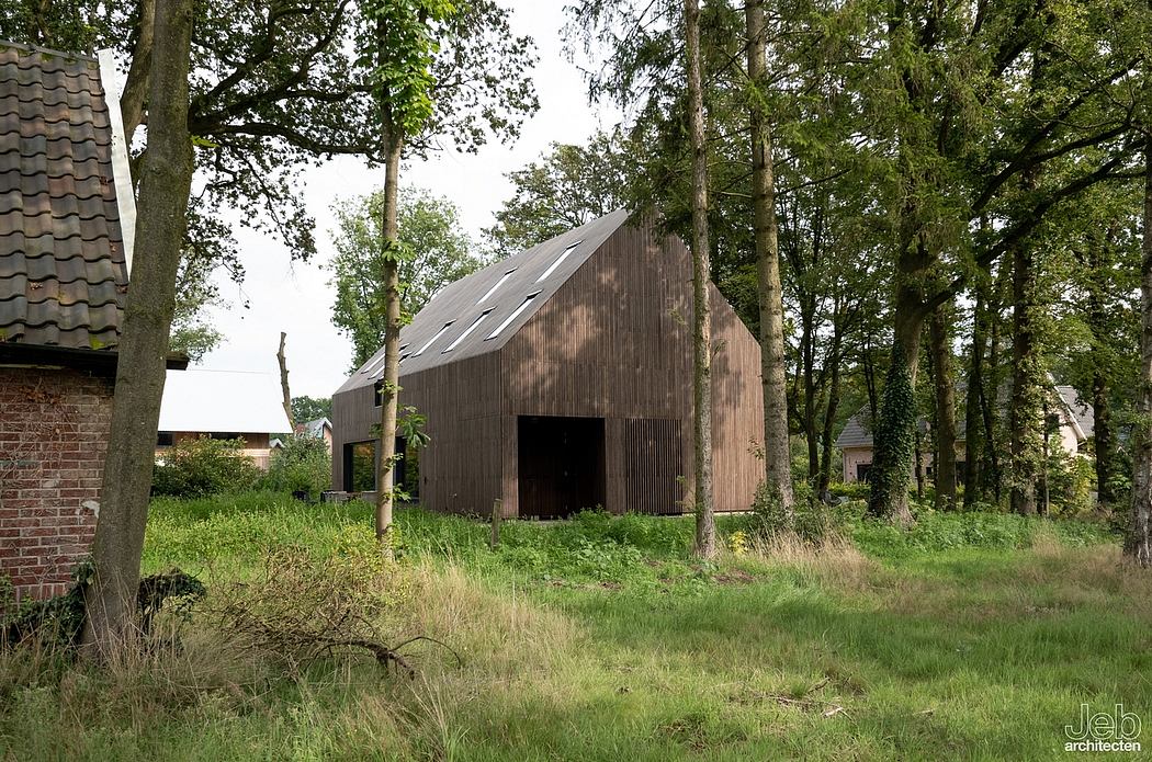 A rustic wooden barn nestled in a lush, green forest setting, with a pitched roof and open facade.