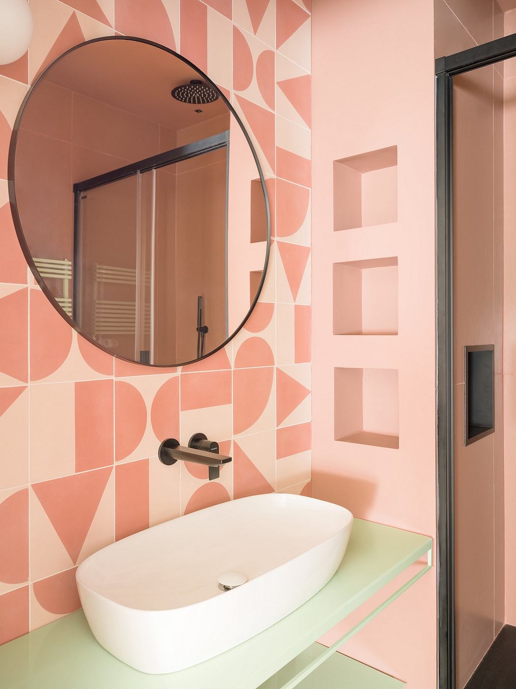 A modern bathroom with a circular mirror, geometric tile patterns, and recessed shelving.