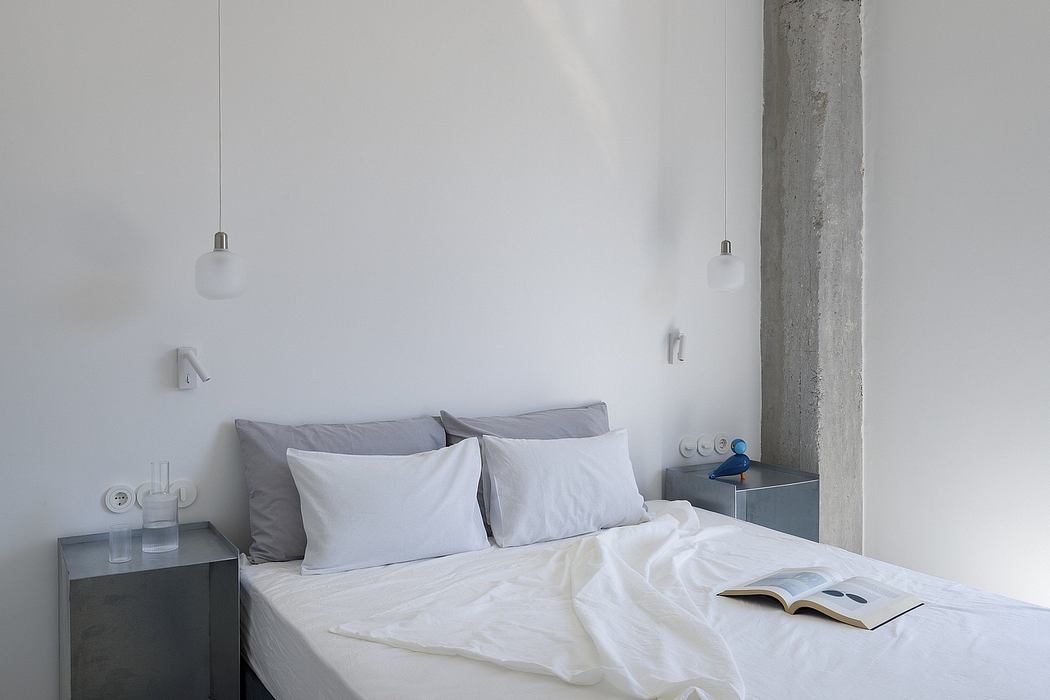 A minimalist bedroom with concrete walls, white bedding, and suspended light fixtures.