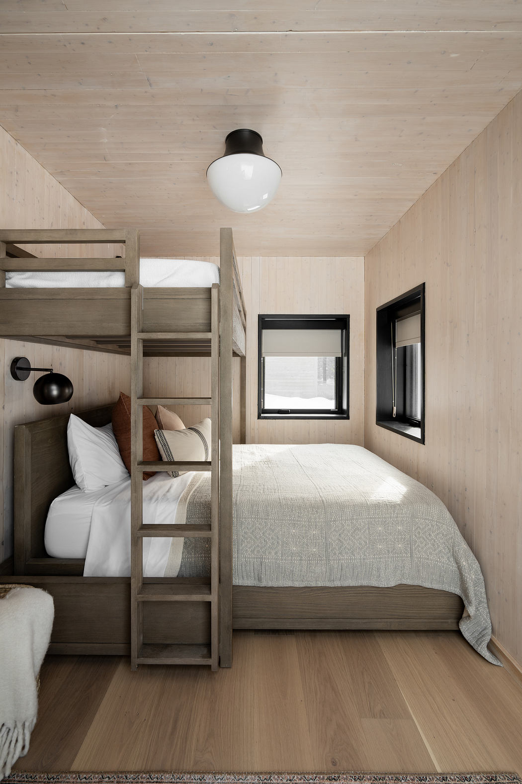A cozy cabin bedroom featuring a bunk bed, minimalist decor, and large windows.