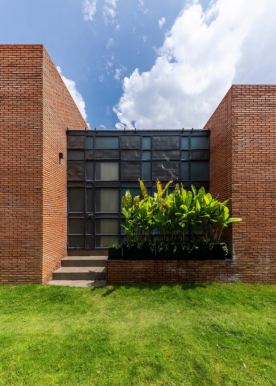 A modern brick building with large windows and a garden planter on the facade, contrasted by lush greenery.