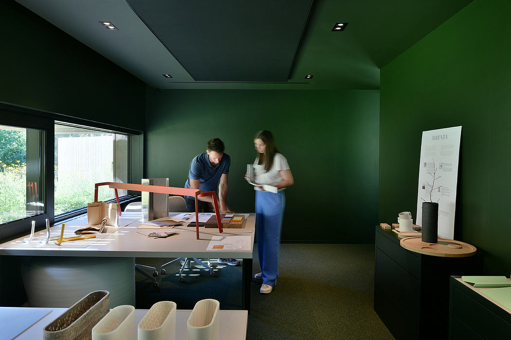 Sleek, modern workspace with dark green walls, wood furnishings, and two people working.