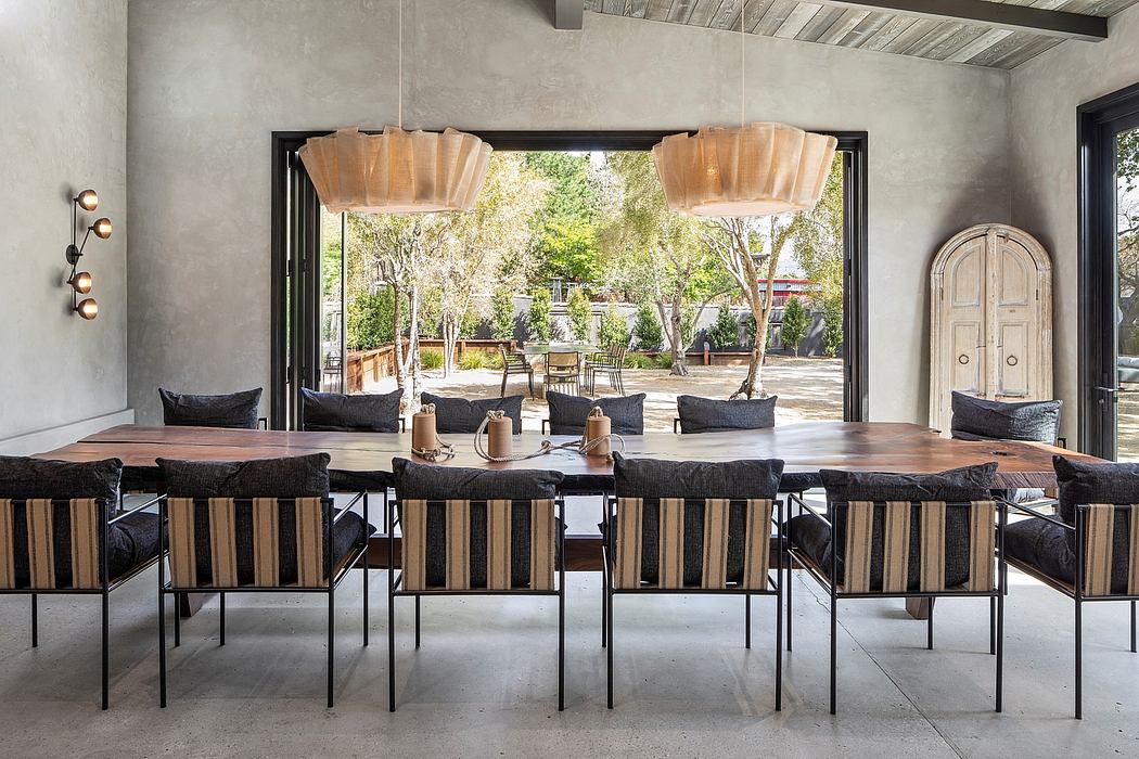 This spacious dining area features a large wooden table, plush seating, and modern lighting fixtures, with a view of the lush outdoor scenery.