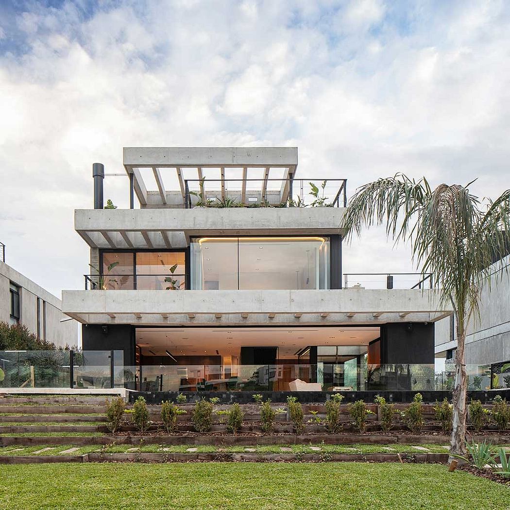 Contemporary concrete residence with expansive glass walls, covered outdoor area, and lush landscaping.