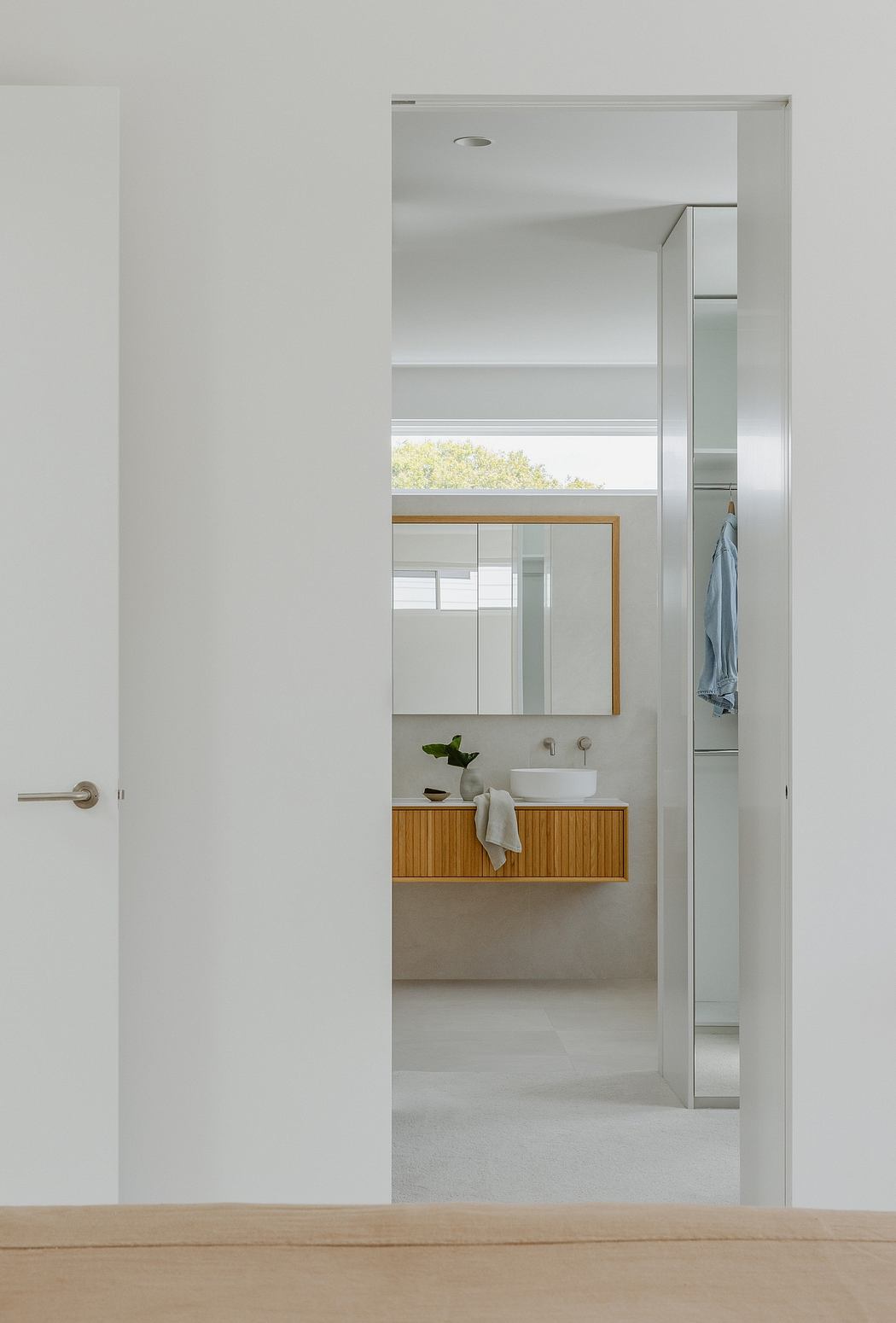 A minimalist bathroom with a wooden vanity, vessel sink, and large mirror framed in metal.