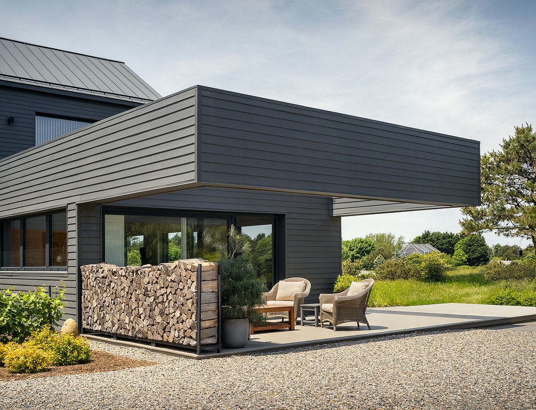 Contemporary rural home with gray siding, extended roof, and outdoor patio with firewood storage.