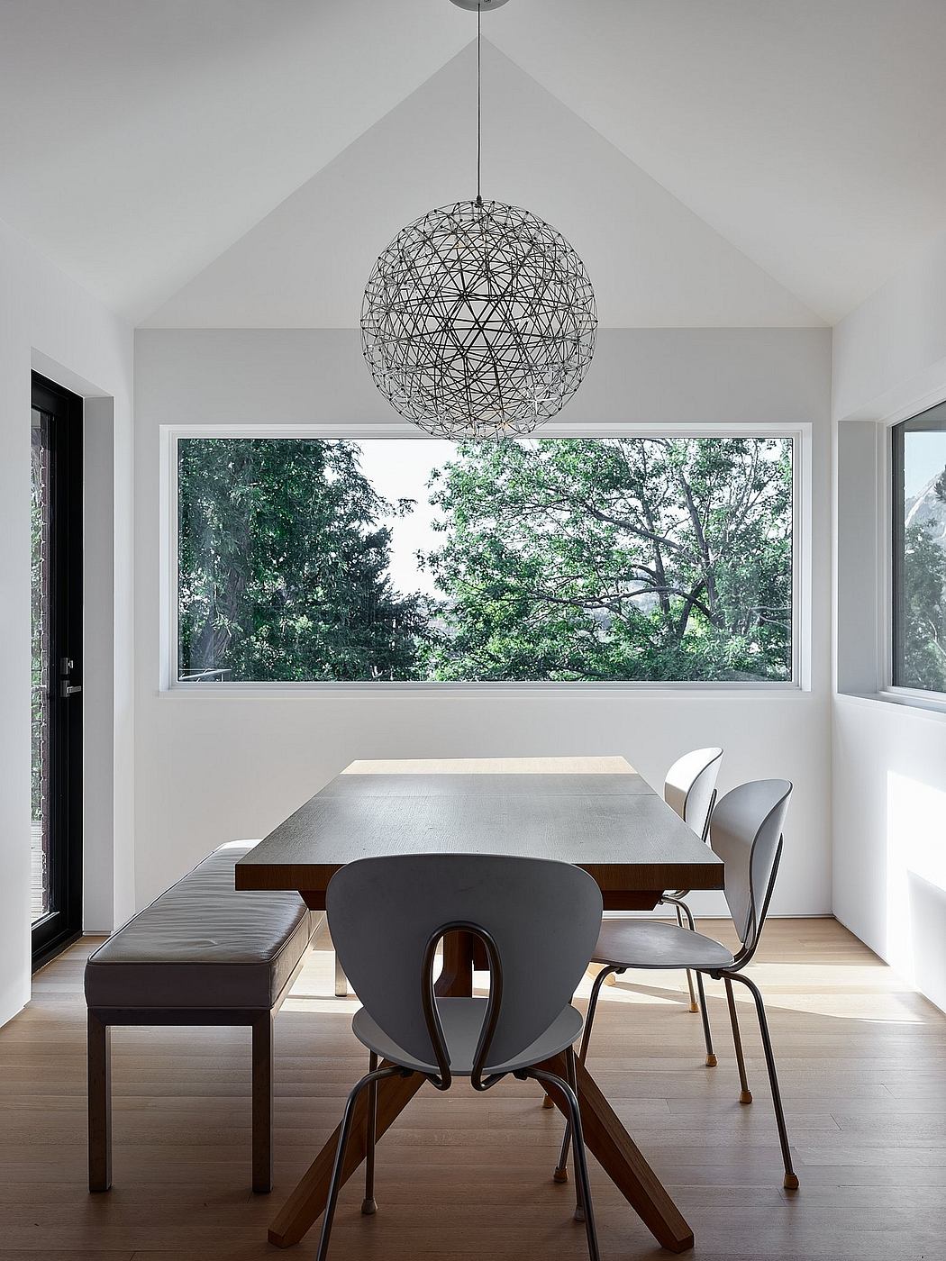 Modern dining room with geometric light fixture, wooden table, and views of lush greenery.