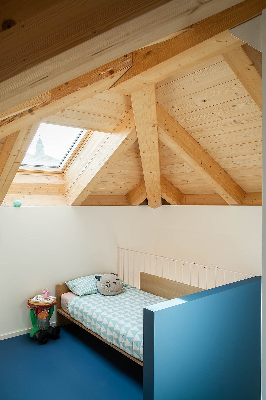 Cozy attic bedroom with wooden beams, skylight, and vibrant blue bed frame.