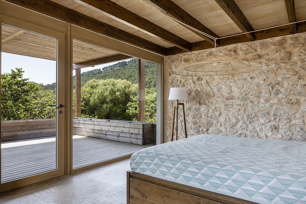 Rustic bedroom with stone walls, wood beams, and large sliding glass doors overlooking nature.