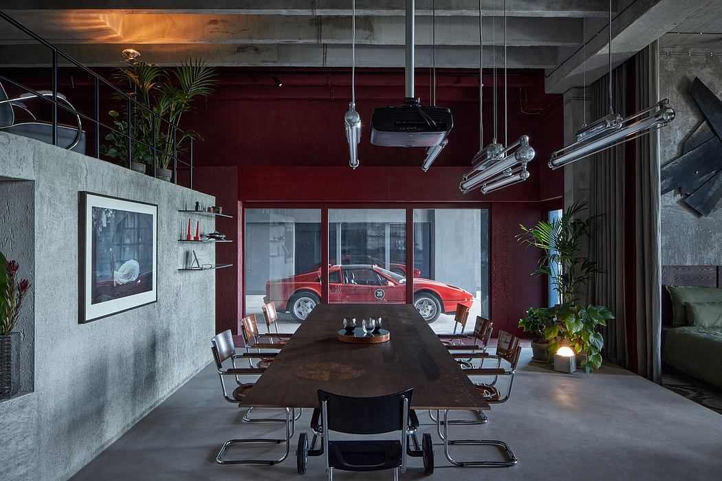 A modern, industrial-style meeting room with a large wooden table, hanging lights, and a red sports car visible through the window.