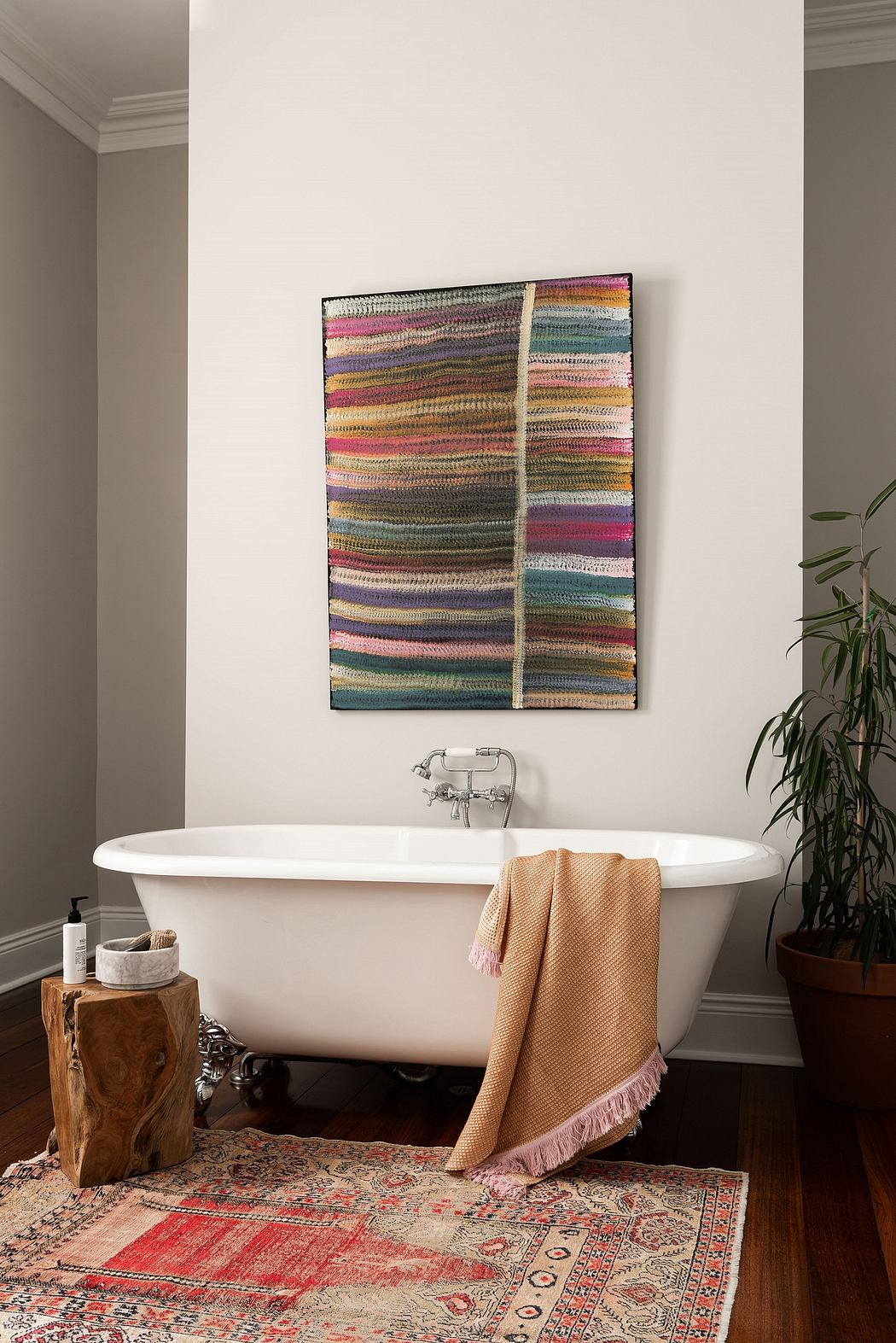 A cozy, earthy-toned bathroom with an ornate rug, freestanding tub, and textured wall art.