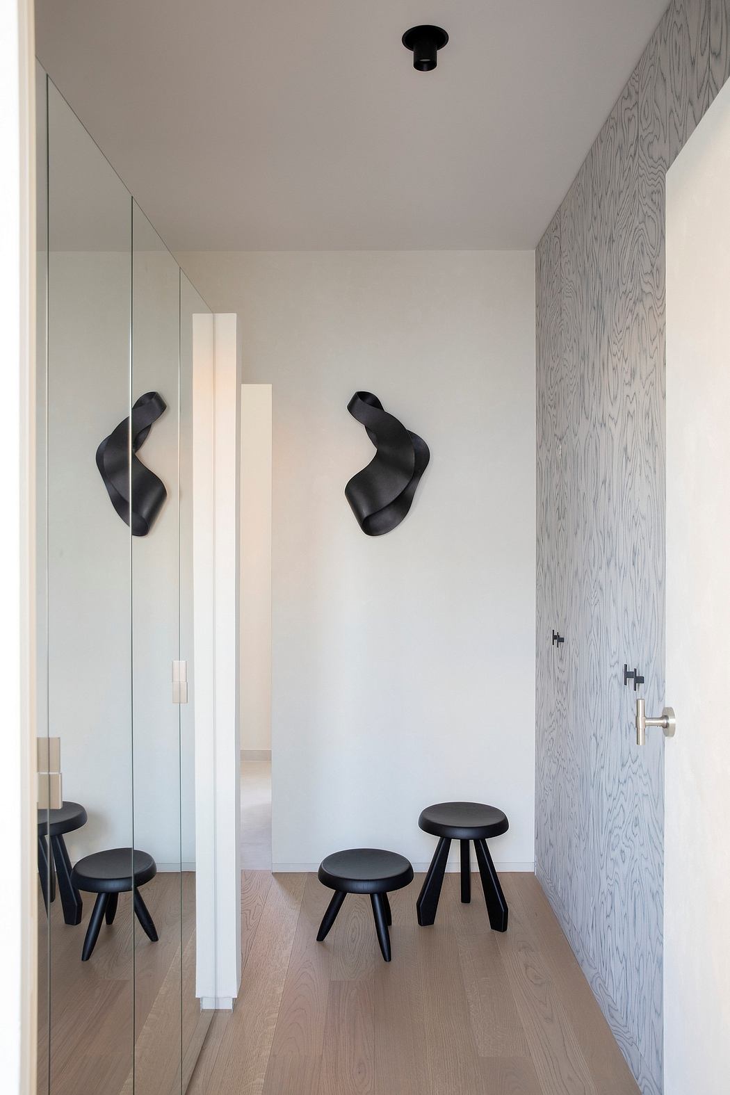 Minimalist foyer with curved black sculptures, stools, and modern wood paneling.