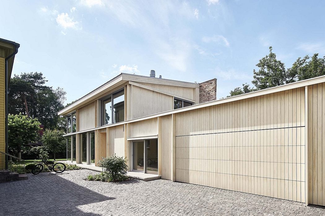 A modern, minimalist exterior with a mix of wood paneling and large windows, surrounded by lush greenery.