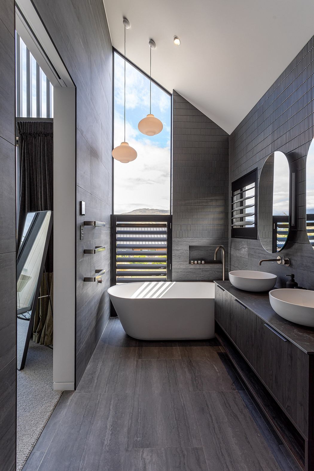Sleek, modern bathroom with large window, freestanding tub, and pendant lighting.