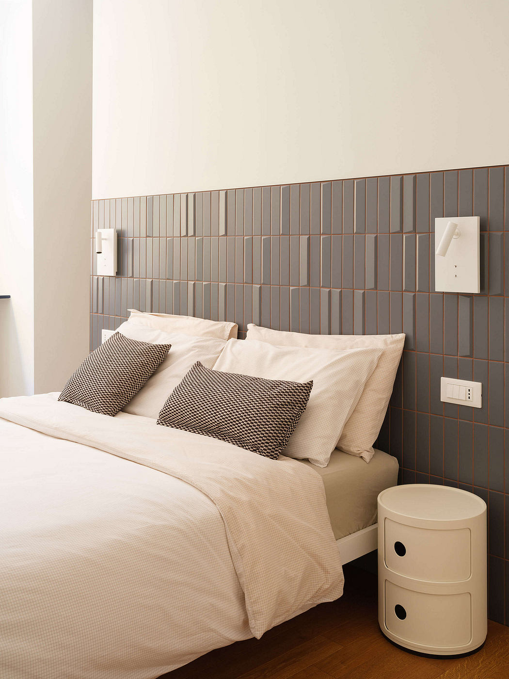 Minimalist bedroom design with gray tile backsplash, neutral bedding, and modern nightstand.