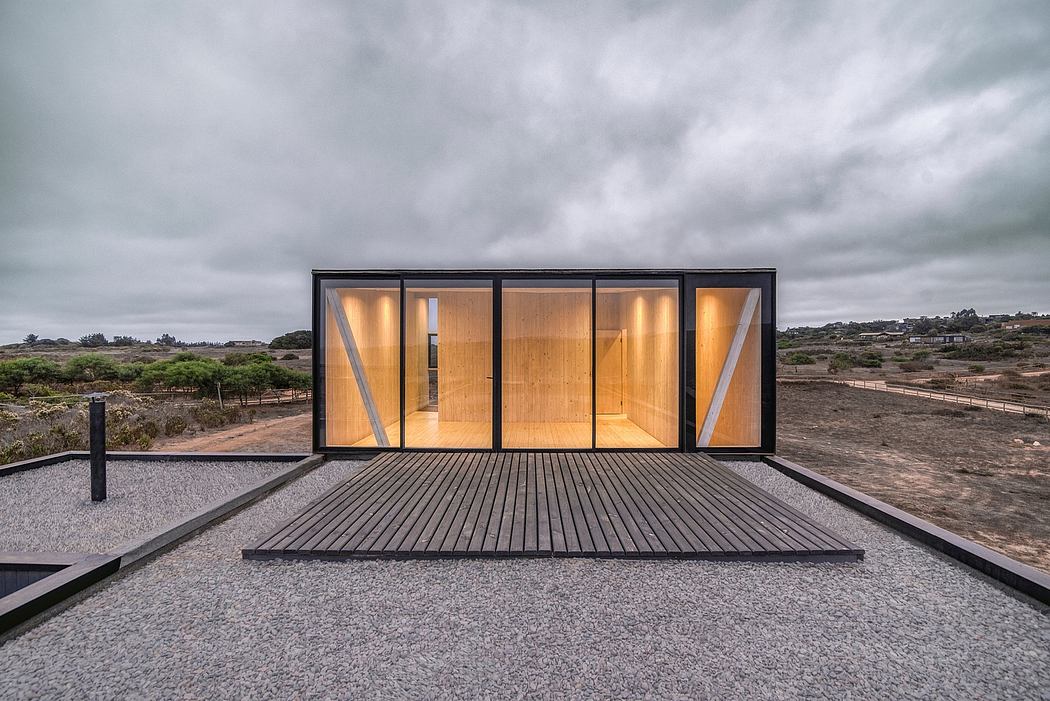 A modern, glass-walled cabin with a wooden interior, situated on a gravel patio.
