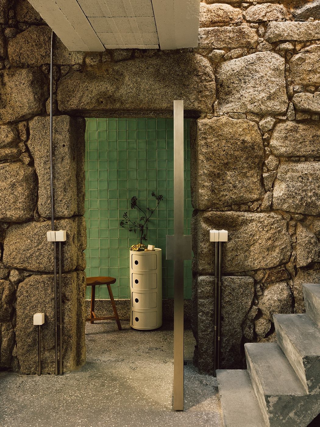 A rustic bathroom with green tile, stone walls, and minimalist furnishings.