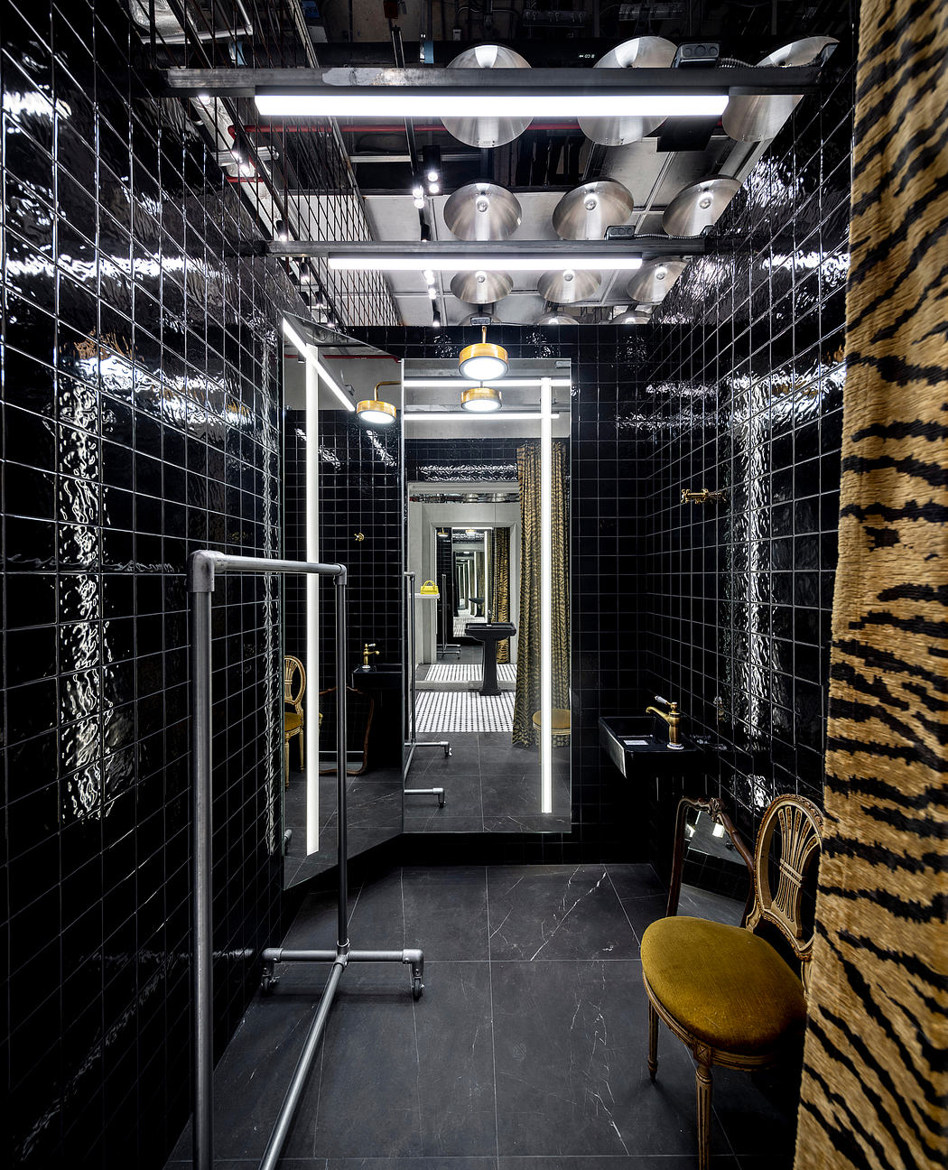 Striking industrial-style hallway with black tiles, metallic fixtures, and a yellow accent chair.