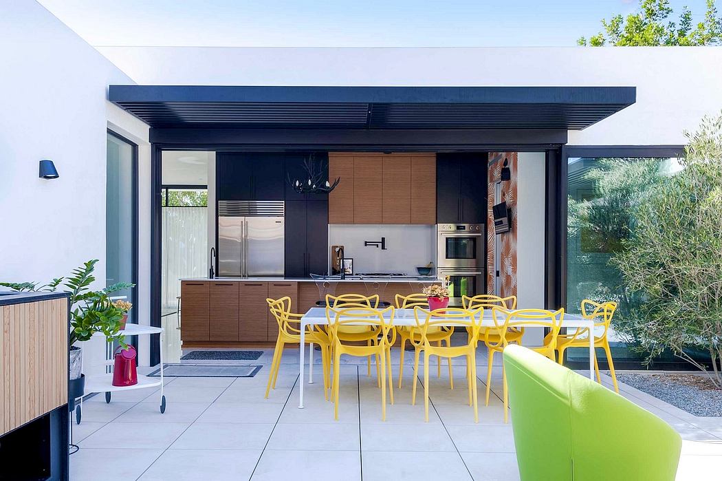 Modern open-plan kitchen and dining area with sleek black and wood cabinetry, and vibrant yellow chairs.