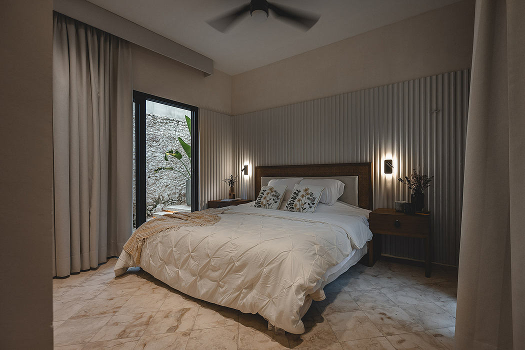Cozy bedroom with wooden headboard, plush bedding, and large window displaying lush greenery.