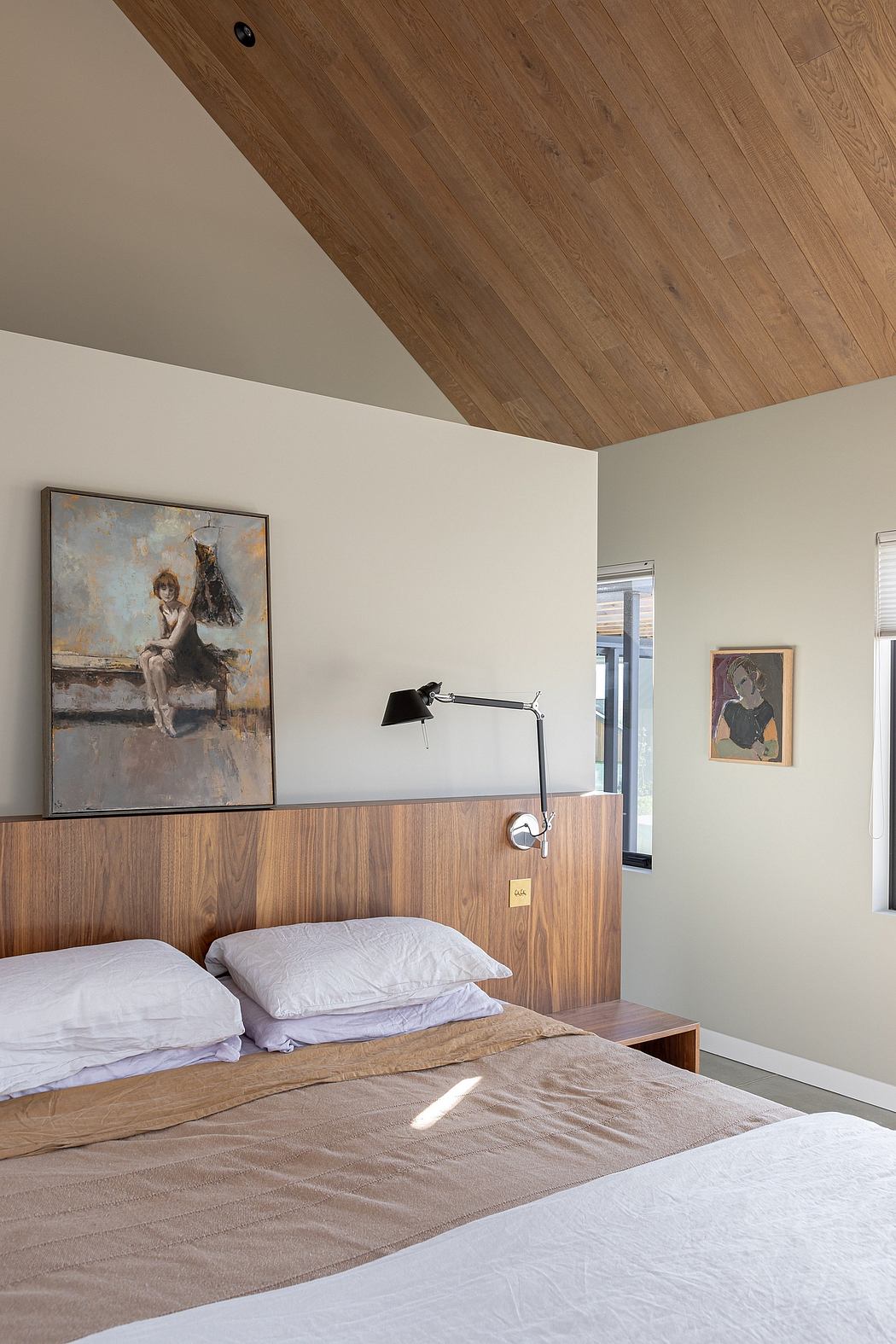 The bedroom features a wooden vaulted ceiling, artwork, and a modern lamp design.