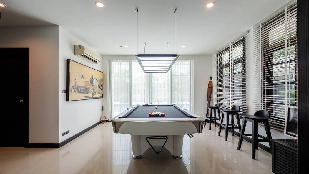 Sleek, modern game room with pool table, bar stools, and large windows overlooking outdoor greenery.