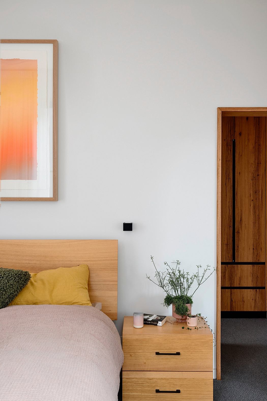 A cozy bedroom with a wooden bed frame, bedside table, and framed artwork on the wall.