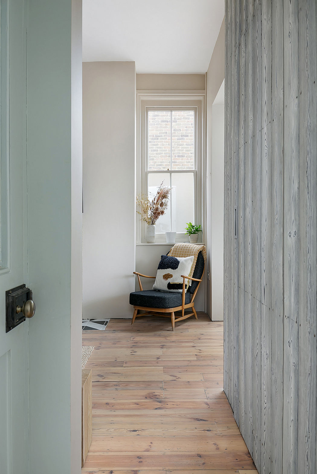 A cozy nook with a wooden armchair, plants, and natural lighting through a window.