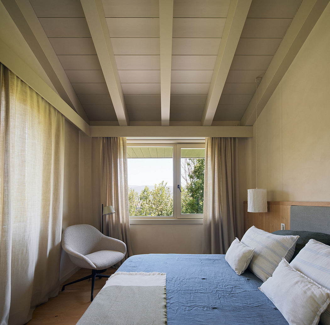 Cozy bedroom with exposed wooden beams, large window overlooking lush greenery.