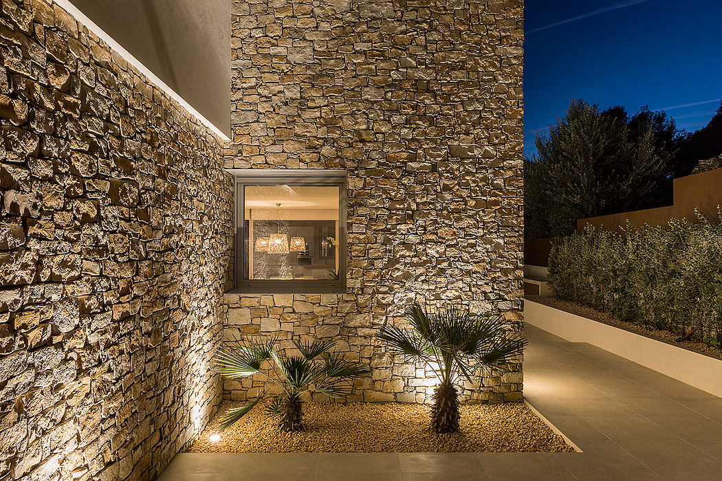 Stunning stone facade with recessed lighting, framed window, and tropical landscaping.