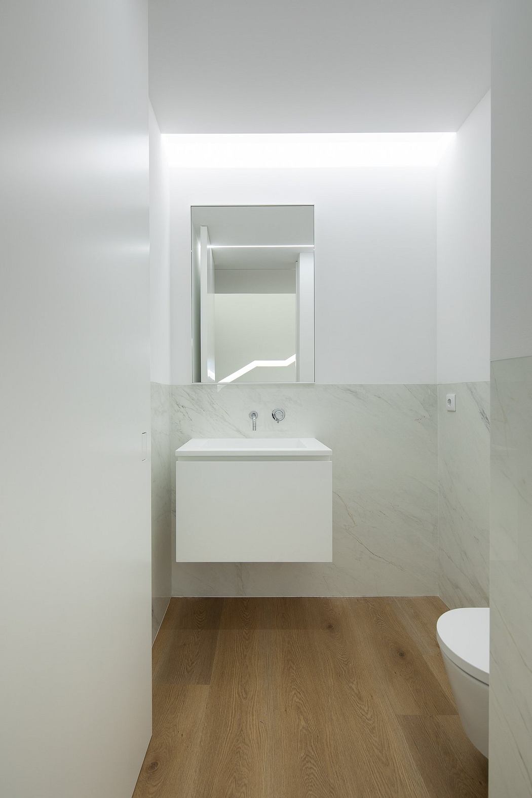 Modern, minimalist bathroom with white vanity, marble wall, and wooden floor.