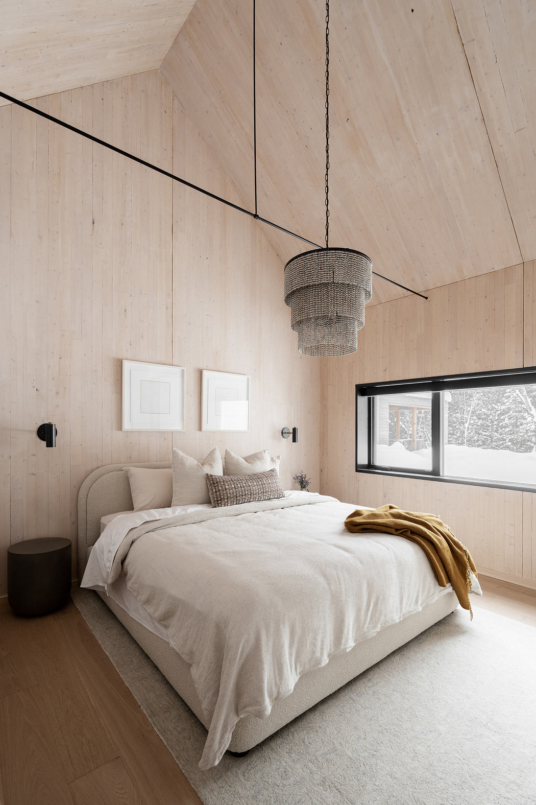 Minimalist bedroom with wood-paneled walls, large window, and metal chandelier.
