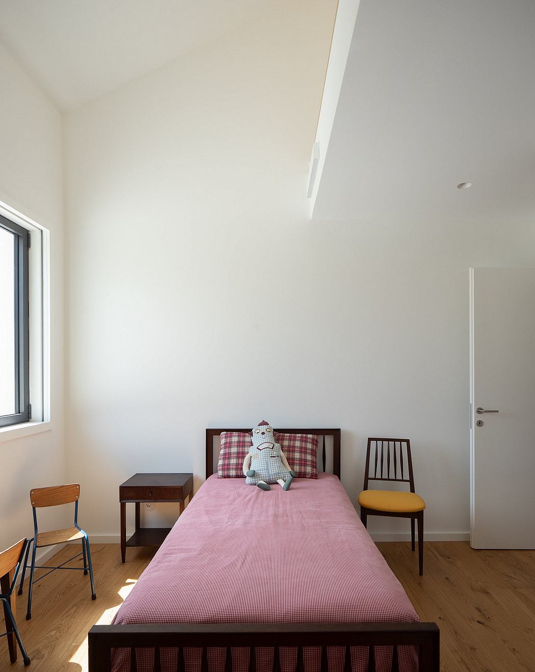 Minimalist bedroom with wood furniture, checkered bedding, and a plush toy on the bed.