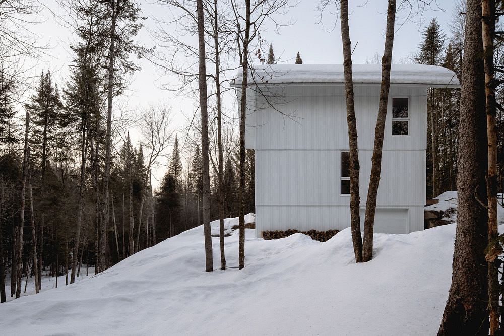 A modern winter cabin nestled in a snowy forest, with a distinctive domed roof and large windows.