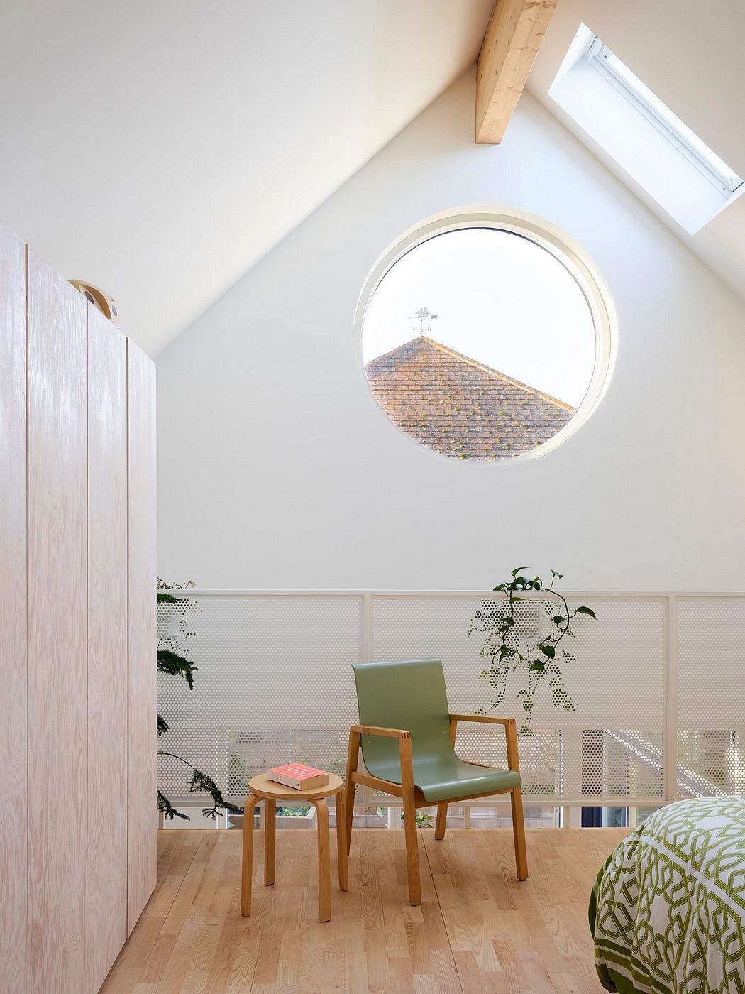 Bright, minimalist room with round window overlooking a tiled roof, wooden furnishings.