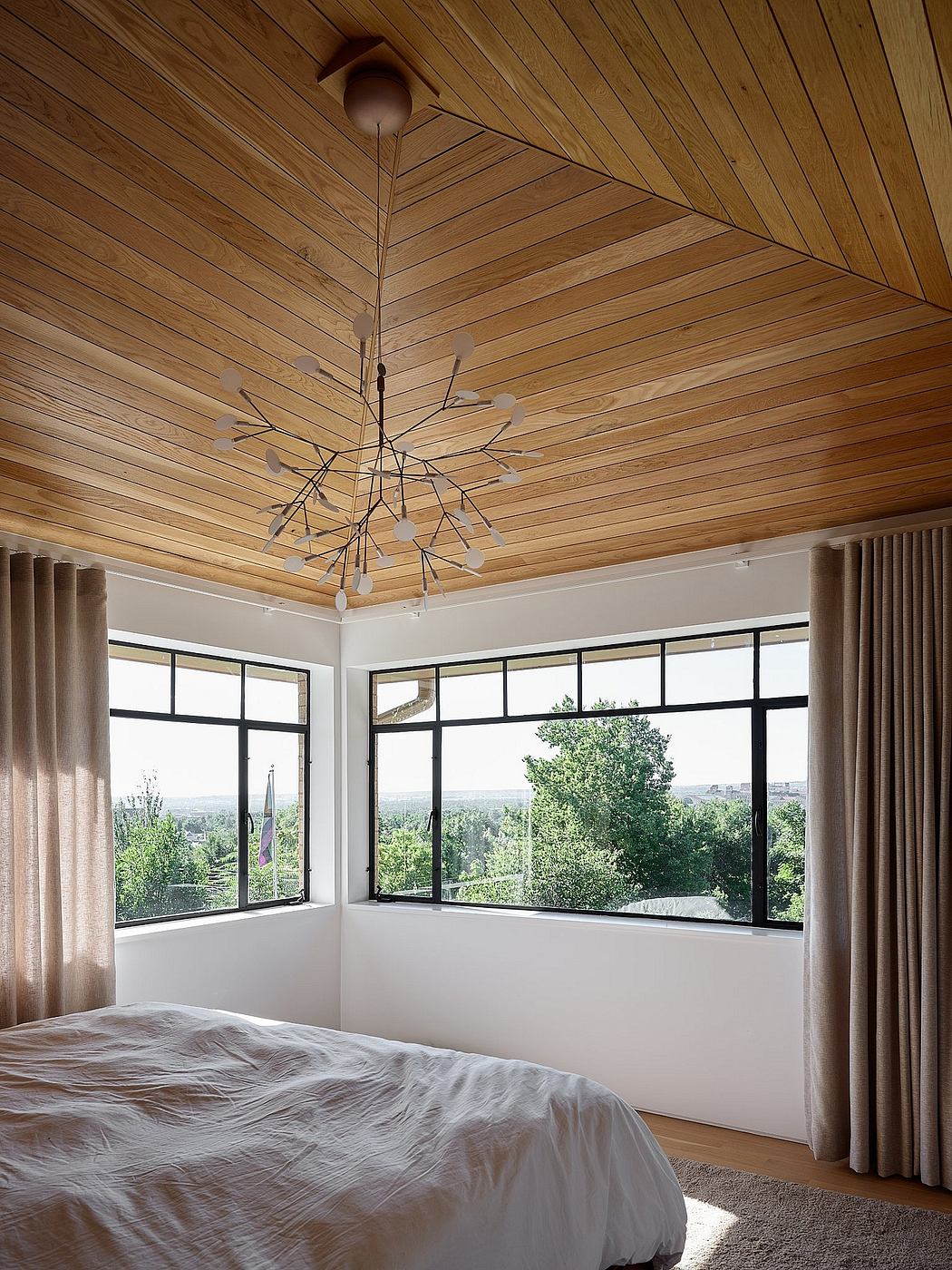 Warm-toned wooden ceiling with modern light fixture, floor-to-ceiling windows offering scenic views.