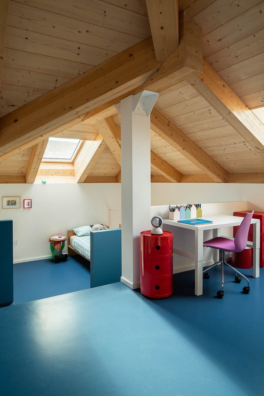 A cozy attic room with a wooden ceiling, desk, and colorful furniture.