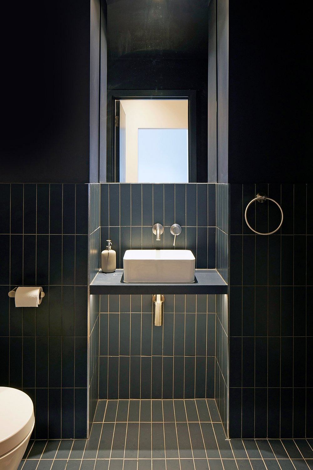 Modern, minimalist bathroom with dark tiles, rectangular sink, and brass fixtures.