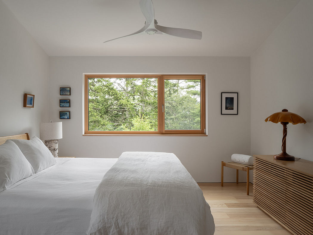 Cozy bedroom with wooden framed windows overlooking lush greenery, modern ceiling fan.