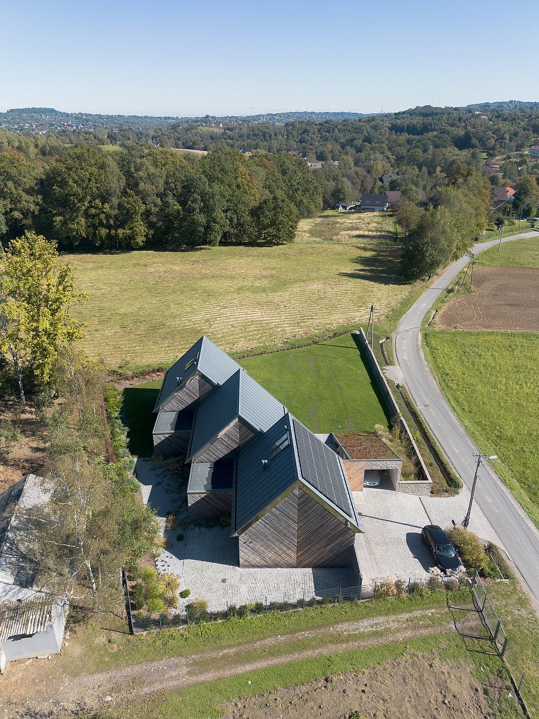 Modern architectural home with angular roofs and wood siding, surrounded by lush greenery.